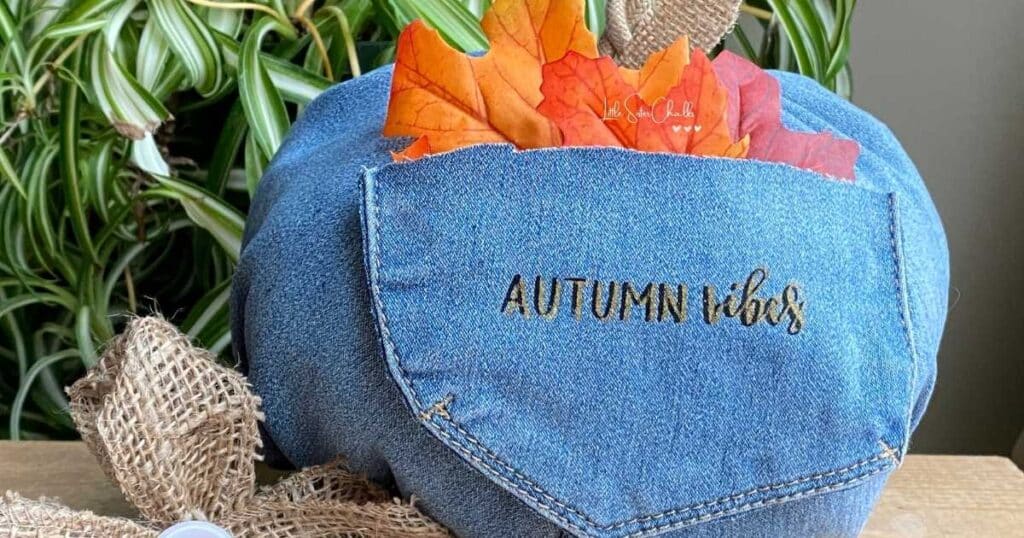 Denim pumpkin with pocket holding red and orange fall leaves with the words "autumn vibes" chalked in black ink offset with the same words chalked in gold ink for blog post Giving Your Stencil a Little Shift Creates the Chalk Couture Shadow Effect