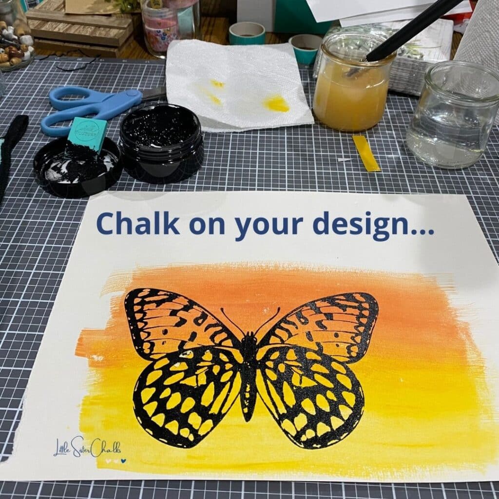 Photo of watercolor paper watercolored in orange and yellow ombre effect with a butterfly chalked in black chalk paste with the words "chalk on your design" for the blog post Try Your Hand at Watercoloring with Chalk Couture