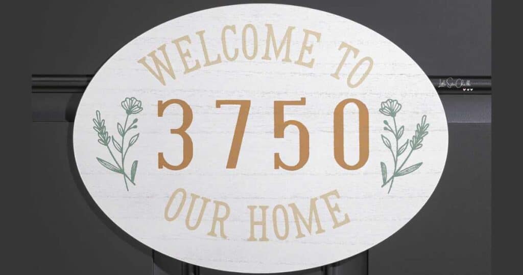 A white oval door sign with the words "Welcome to our home" with "3750 in the center flanked by flowers chalked in green for the blog post Tips for Updating Your Entryway