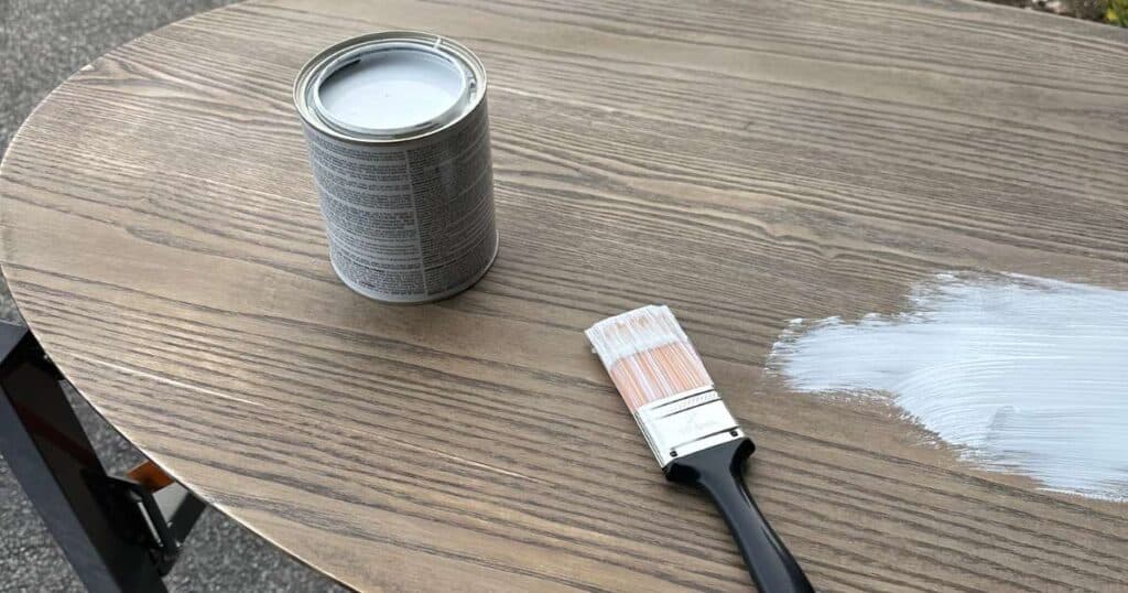 The top of a coffee table with a can of open primer and a paint brush with a bit of the primer applied to the table for the blog post "Lending a Helping Hand with Crafts for Charity".