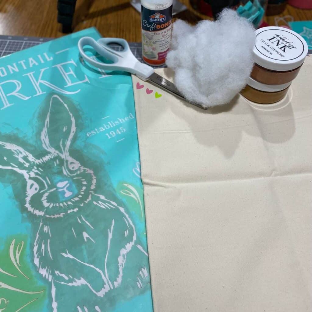 Supplies including a bunny stencil, canvas fabric, scissors, cotton stuffing, 2 jars of Shimmer Copper Chalk Couture Chalkology Ink, and fabric glue for the blog post "Nine Ways to Use a DIY Stuffed Bunny in Your Decor this Spring".