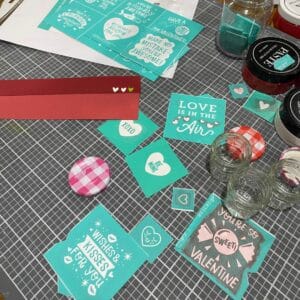 Mini Valentine's Day stencils, empty mini jars, red construction paper on a craft mat for the blog post "Mini Jam Jar Craft Ideas".