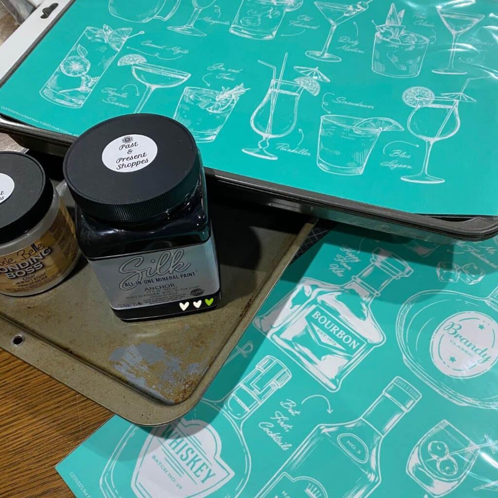 Old cookie sheets, Dixie Bell bonding boss and Silk paint in Anchor and Chalk Couture stencils with cocktails and alcohol bottles on a table for the blog post "How to Upcycle an Old Cookie Sheet with Chalk Couture".