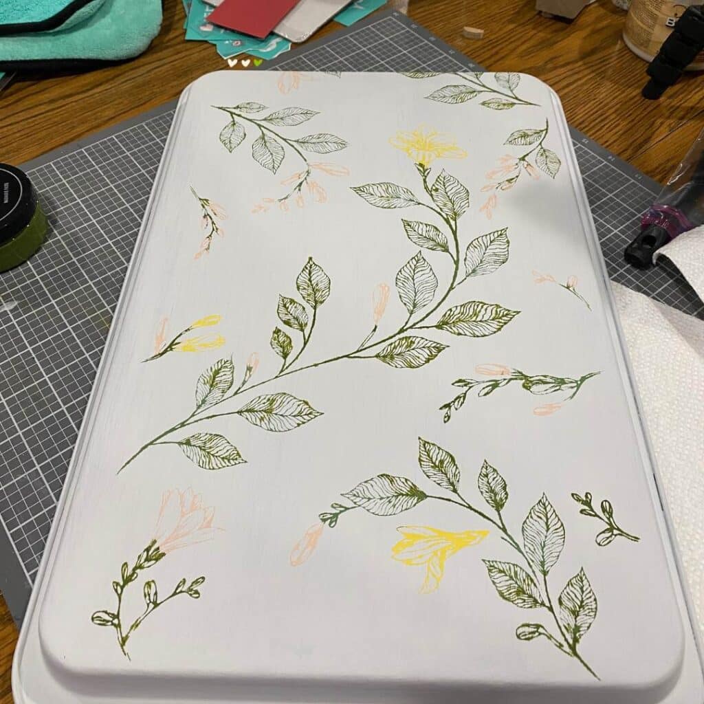 An old cookie sheet painted white with the Chalk Couture Dragonfly Vines stencil applied in yellow, peach and green chalk paste to transform it into a memo board for the blog post "How to Upcycle an Old Cookie Sheet with Chalk Couture".
