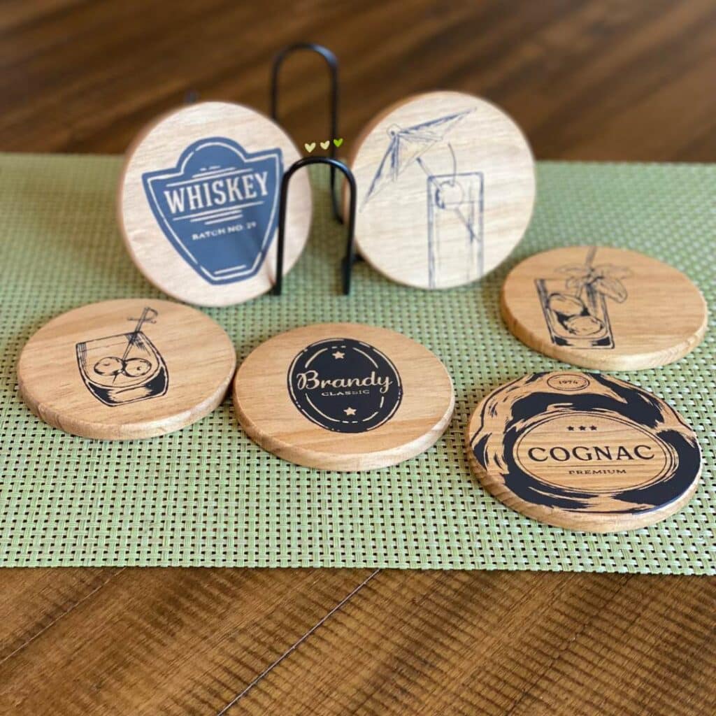 A set of six wood coasters on a table with cocktail designs including a whiskey label, a brandy label, a cognac label and three drink images for the blog post "Bar Cart Decor Ideas that will have You Raising Your Glass".