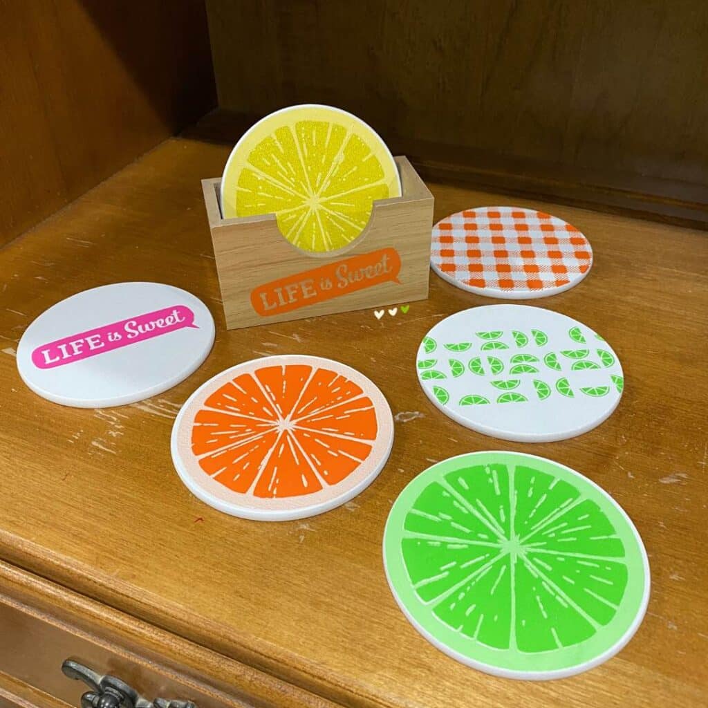 A completed set of Chalk Couture coasters decorated with the Sweet Citrus stencil including one of each of the following coasters: a slice of lime, a slice of orange, a slice of lemon, "life is sweet", a checkerboard pattern, and a small citrus pattern for the blog post "Bar Cart Decor Ideas that will have You Raising Your Glass".