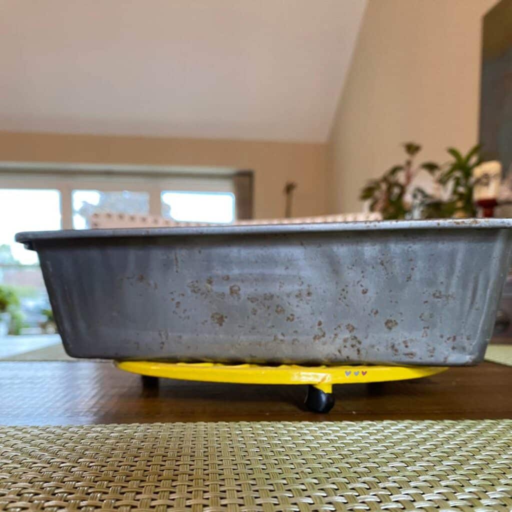 A photo of an old bread pan on a yellow trivet on a table for the blog post "Simple Baking Pan Crafts You Can Use to Repurpose Your Old Bakeware".