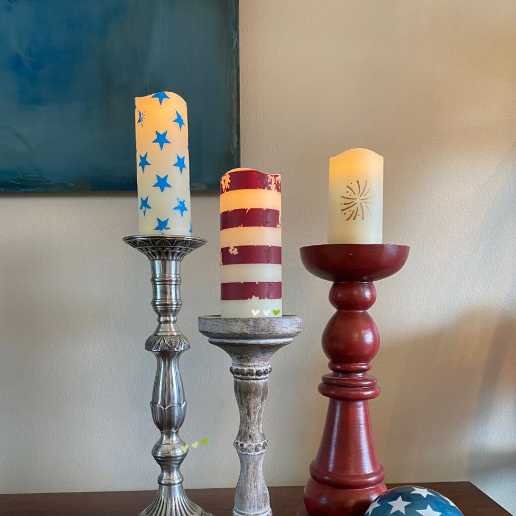 A set of 3 flameless candles on candlesticks decorated with blue stars, red strips and a gold firework using Chalk Couture stencils for the blog post "Fly the Red, White & Blue with the 2024 Patriotic Collection from Chalk Couture".