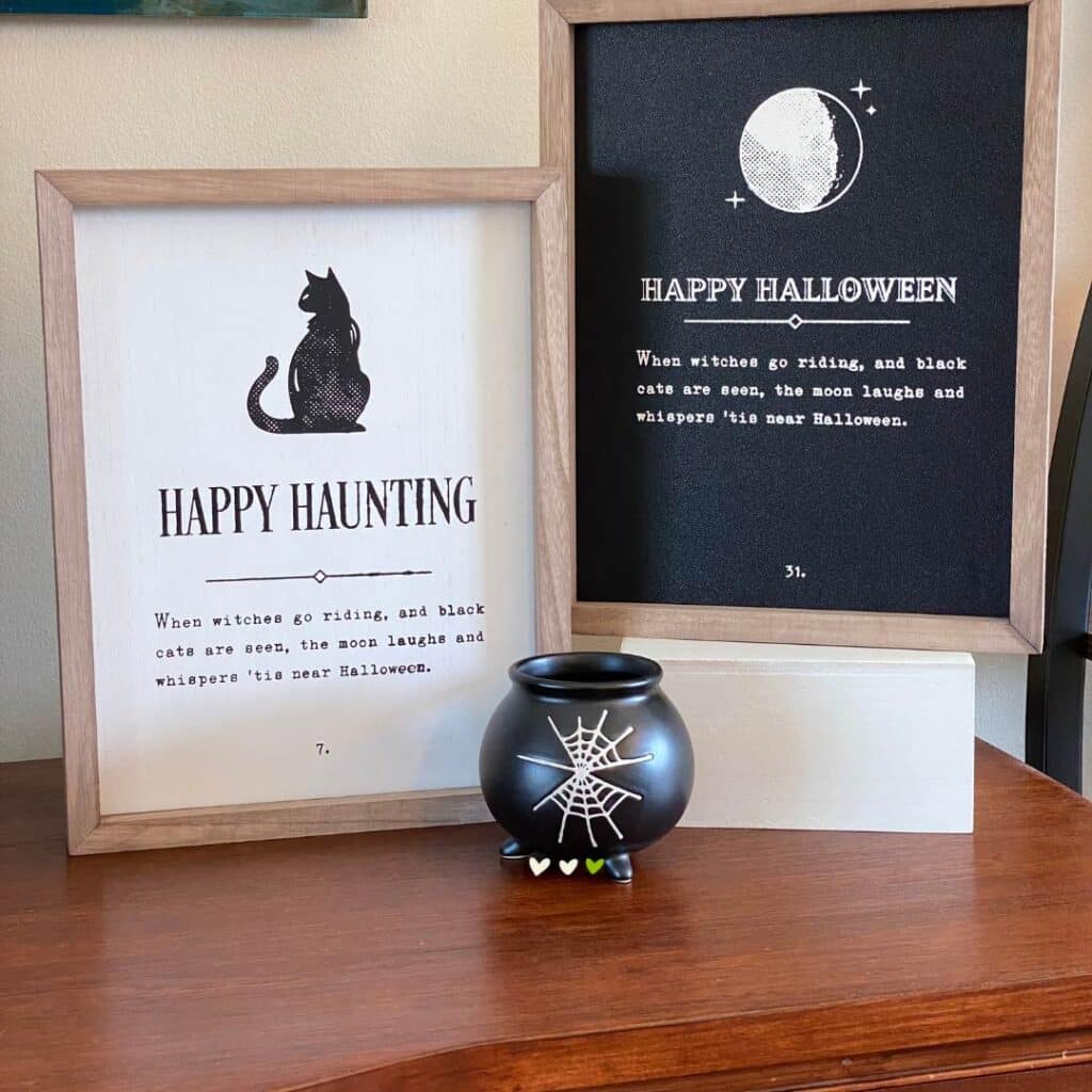 Two Chalk Couture Outside the Box Frames on a sideboard, one with a white center and one with a black center with Halloween sayings from the Chalk Couture Happy Haunting stencil, with a black cauldron cup with white spider webs in front of the box frames for the blog post "Theme It Up for Halloween".