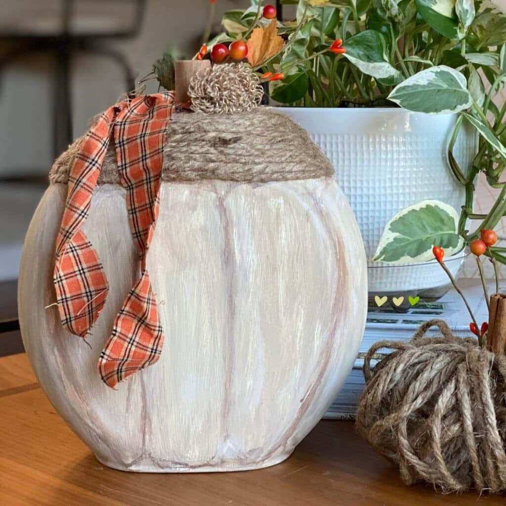 A photo of a pumpkin made from a Tide Pod container done with paint and embellished with twine, a fabric scrap ribbon, and burlap flowers for the blog post "Three Easy DIY Pumpkin Crafts".