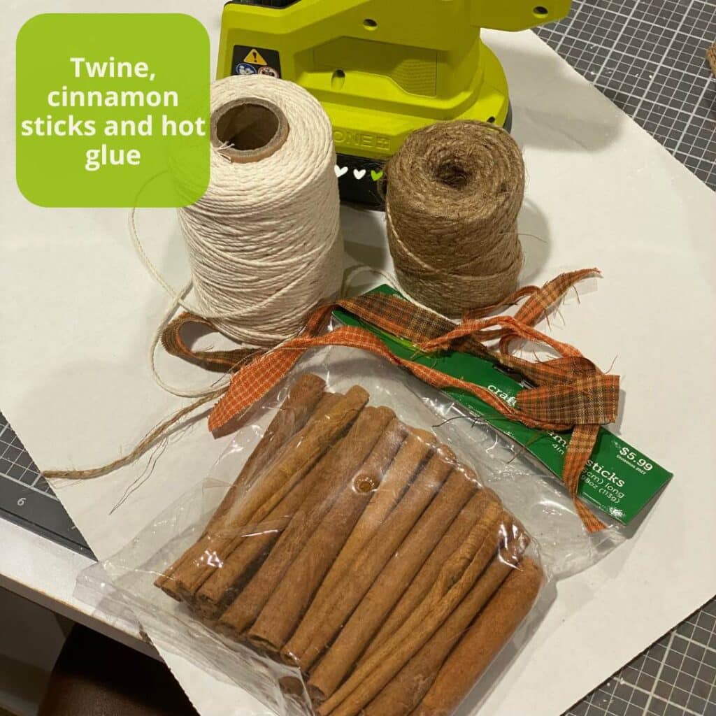 A photo of supplies on a craft mat that are needed to make twine pumpkins including a hot glue gun, twine, cinnamon sticks and fabric scraps for the blog post "Three Easy DIY Pumpkin Crafts".