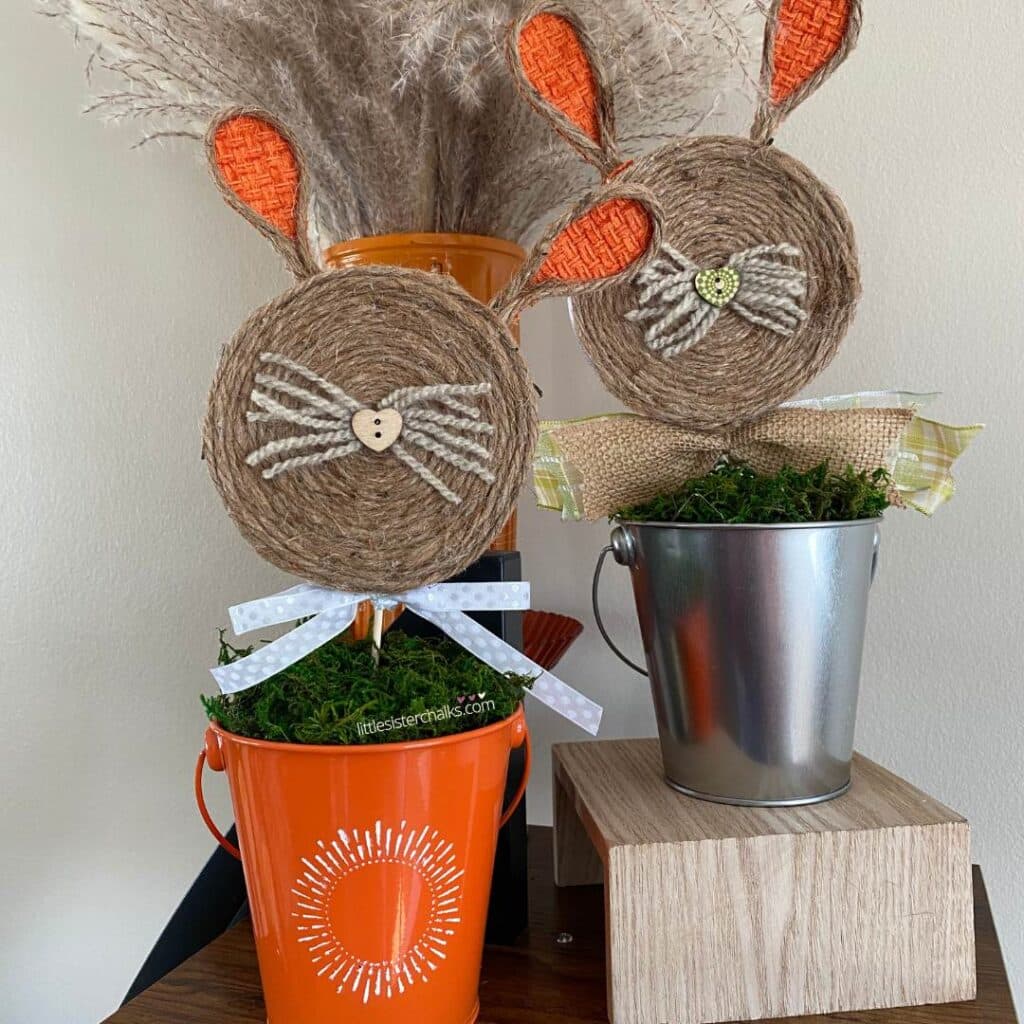 A photo of two bunnie made from cheese containers; one in an orange buck and one in a silver bucket for the blog post "Crafting Beyond the Bin: Adorable Bunny in a Bucket Upcycle from a Laughing Cow Cheese Container".