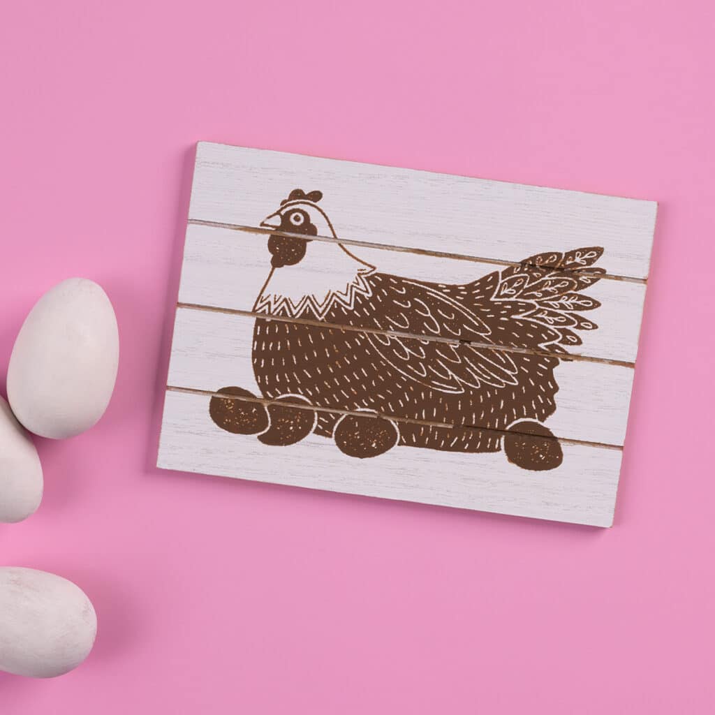 A photo of the finished project using the Chalk Couture Mother Hen Try Me Kit with a hen and eggs chalked in Espresso Chalkology Paste on a shiplap sign flanked by three white eggs for the blog post "Try your hand at chalking with a Chalk Couture Try-me Kit".