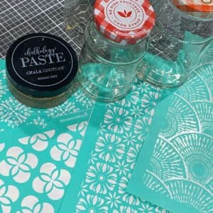 A photo of supplies used for an easy glass jar upcycle project including empty glass jars, Chalk Couture chalk paste, and various stencil designs.