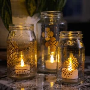 A photo of 3 glass jars turned upcycled into candle holders using Chalk Couture stencil designs for the blog post "Easy Glass Jar Upcycle Project".