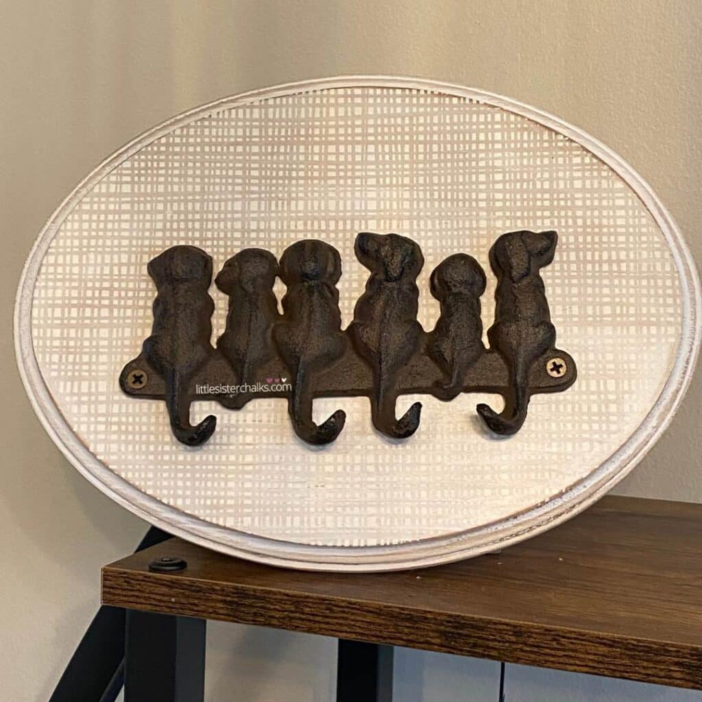 A set of 6 iron dogs with hooks for tails mounted to an oval piece of wood with a woven background chalked on it for the blog post "Decorating with Metals".