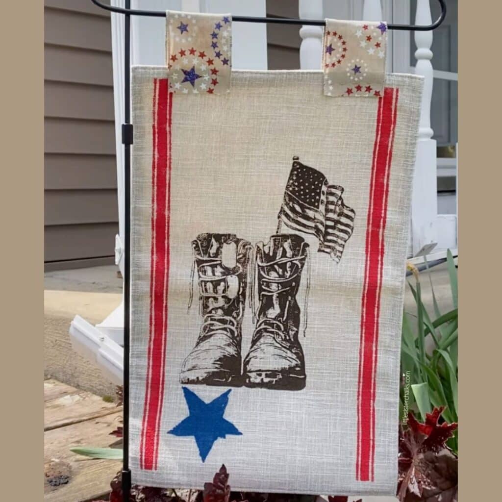 A garden flag with red stripes, a blue star and army boots, dog tags and an American flag inked in brown held by two tabs with red, white and blue stars for the blog post "Outdoor Fabric Accessories".